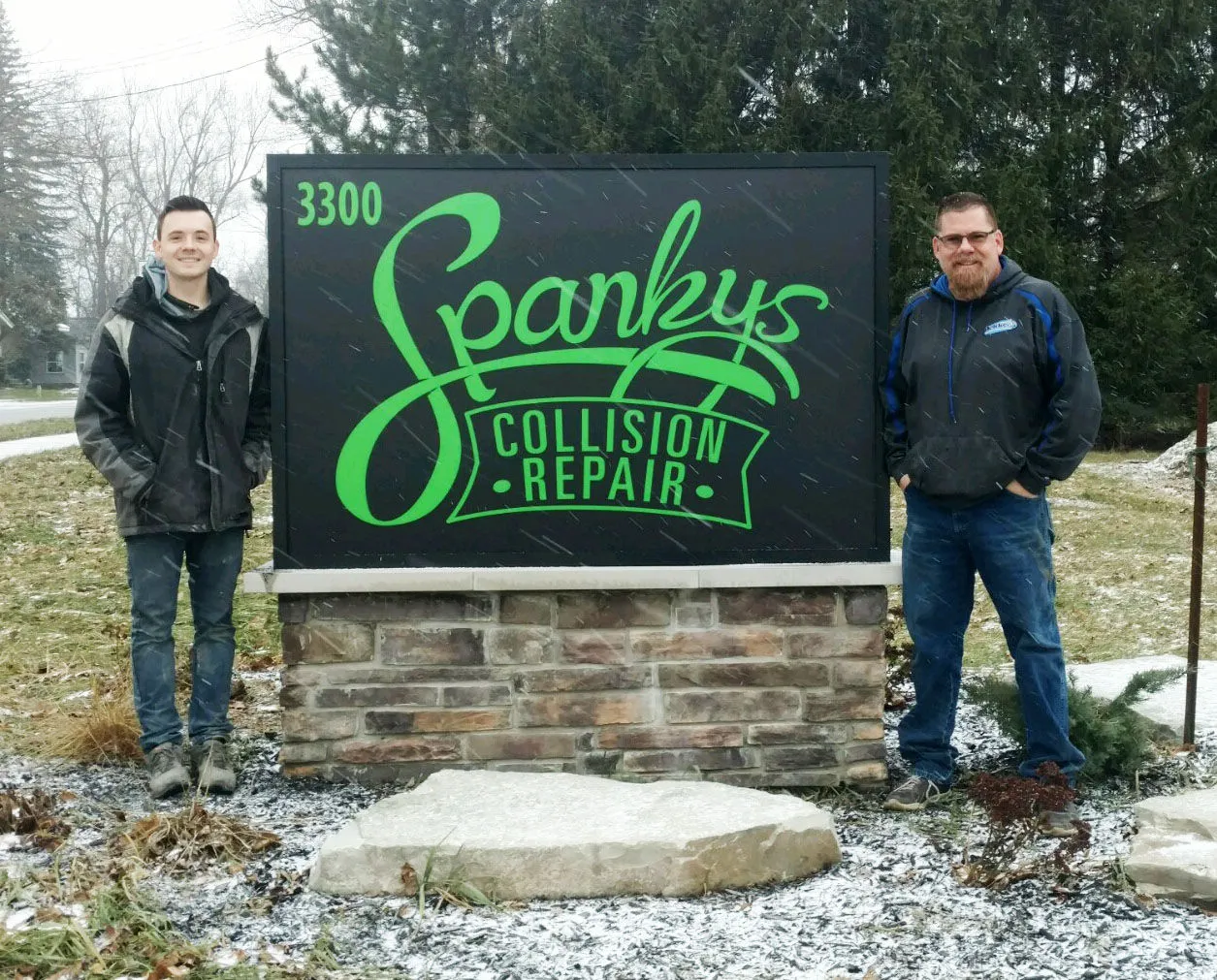 Gordy and Chris Burns beside the Spanky's Collision Repair sign on 24th Ave in Hudsonville, MI
